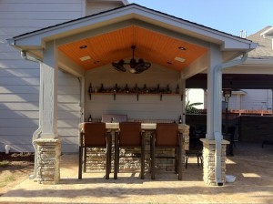 Second "after shot" of outdoor living space design by Outdoor Homescapes of Houston. This covered patio, made possible by a roof extension with a wooden ceiling, features a rusting outdoor bar and grill area. More at www.outdoorhomescapes.com.