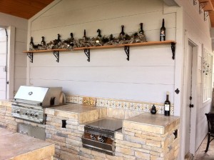 Closeup of a rustic outdoor bar and grill area designed and built by Outdoor Homescapes of Houston. It features a wet bar, RCS grill and double burner, built-in storage, outdoor refrigerator and Kegerator, all in natural stone islands. More at www.outdoorhomescapes.com. 