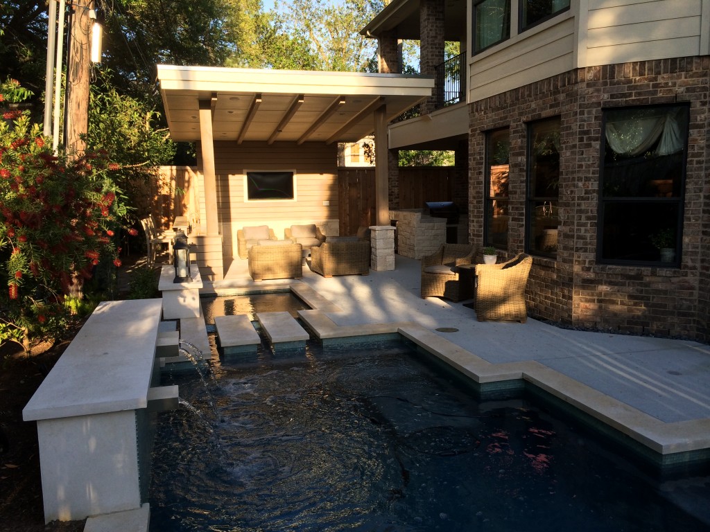 Beautiful built-in pool with fountains next to outdoor living space and outdoor kitchen with silver travertine tile countertop by Outdoor Homescapes of Houston. More at www.outdoorhomescapes.com/blog