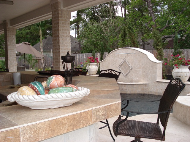 This image of a Houston outdoor kitchen shows a nice tile counter, a water feature (fountain) and counter seating. It's part of a blog post at http://www.outdoorhomescapes.com/outdoor-living-spaces-boost-quality-life-home-values/. For more outdoor living spaces by Outdoor Homescapes of Houston, go to www.outdoorhomescapes.com. 