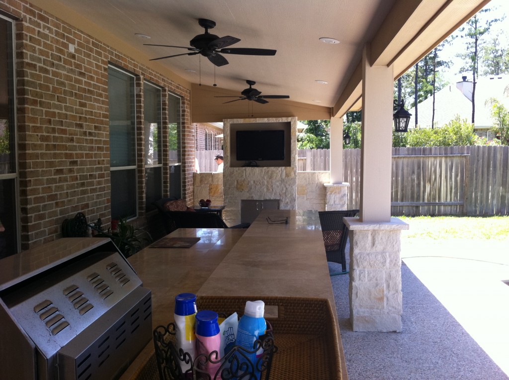 An outdoor media room sits at the far end of this outdoor living space, with an outdoor kitchen in the foreground. Part of a blog post on an outdoor living space designed by Outdoor Homescapes of Houston at www.outdoorhomescapes.com/blog