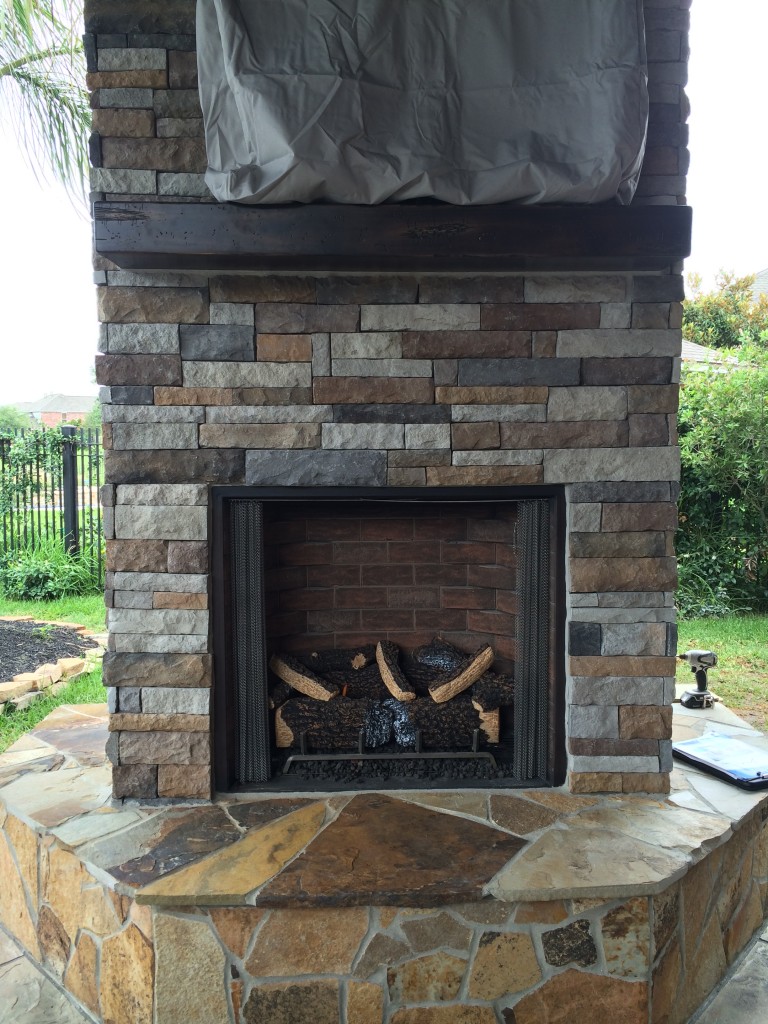 This gas-burning fireplace features a mounted flat-screen TV, drystacked ledgestone walls, a wooden mantel and a flagstone hearth. Designed and built by Outdoor Homescapes of Houston. More at www.outdoorhomescapes.com/blog