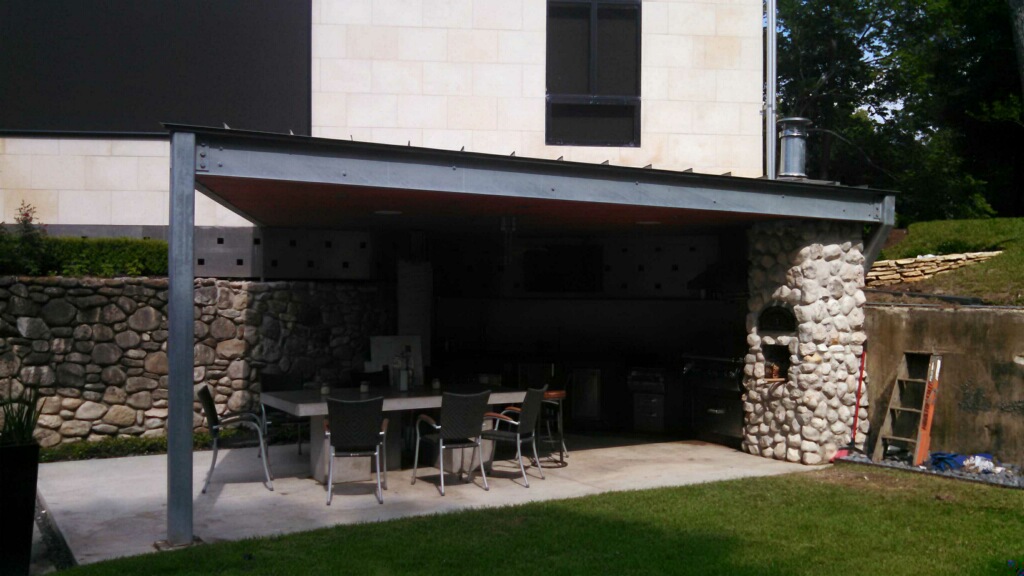 A metal roof with I-beam construction completes this modern outdoor kitchen by Outdoor Homescapes of Houston. More at www.outdoorhomescapes.com