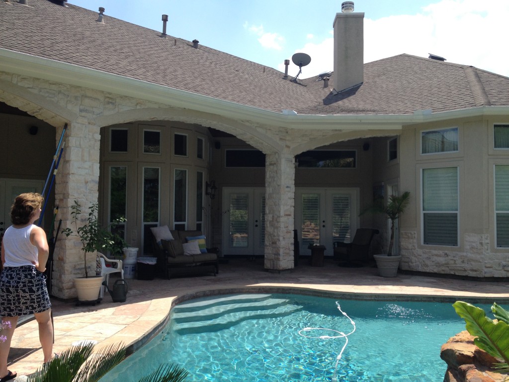 This view of a two-story stone and stucco home in Houston shows the view from a new outdoor sitting area designed and built by Outdoor Homescapes of Houston. The area features an outdoor sitting area next to a cozy fireplace. More at www.outdoorhomescapes.com