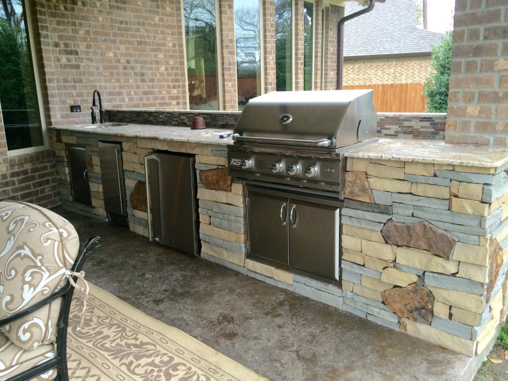 Outdoor living space in Houston is increasingly featuring islands made of natural stone. This covered patio and outdoor kitchen by Outdoor Homescapes of Houston features a mix of three different stones for a unique, customized look. More at www.outdoorhomescapes.com.