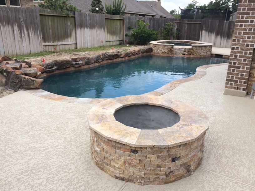 This patio kitchen plan by Outdoor Homescapes of Houston features rustic, naturalistic textures, like a pool with a craggy edge of moss rock boulders and a firepit and spa faced with Scabos split face travertine stone. More details on this project at www.outdoorhomescapes.com/blog 