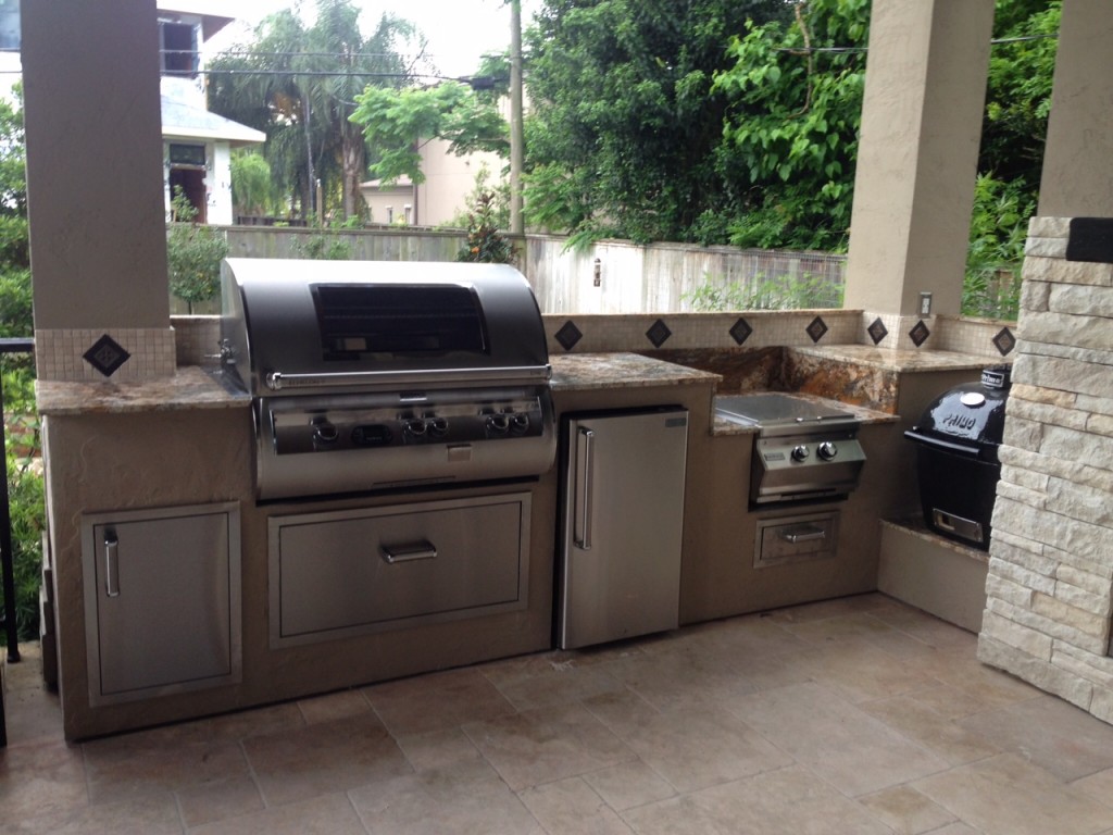 This outside kitchen design idea by Outdoor Homescapes of Houston features a 14-foot-long outdoor kitchen island with a Fire Magic grill, refrigerator, side burner and trash door. A built-in Primo ceramic grill completes the cooking elements. More at www.outdoorhomescapes.com