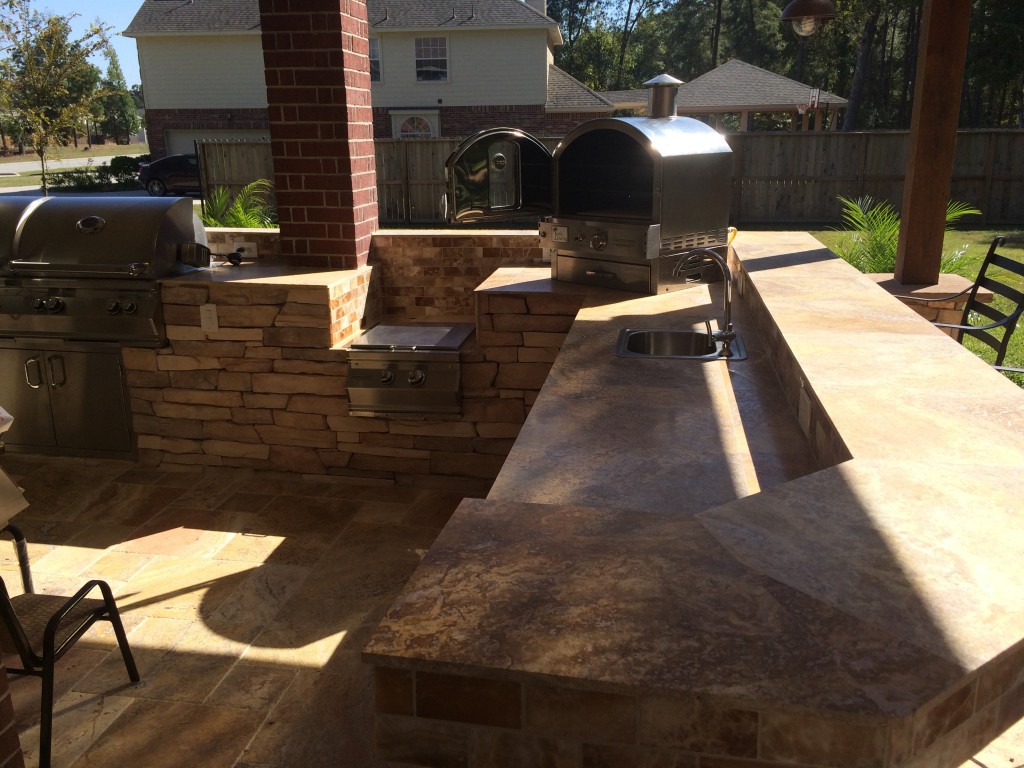 This Houston outdoor kitchen, by Outdoor Homescapes of Houston, features a Pacific Living tabletop pizza oven, Fire Magic charcoal-gas combo grill, a ledgestone island and a silver travertine counter and raised bar. More at www.outdoorhomescapes.com/blog